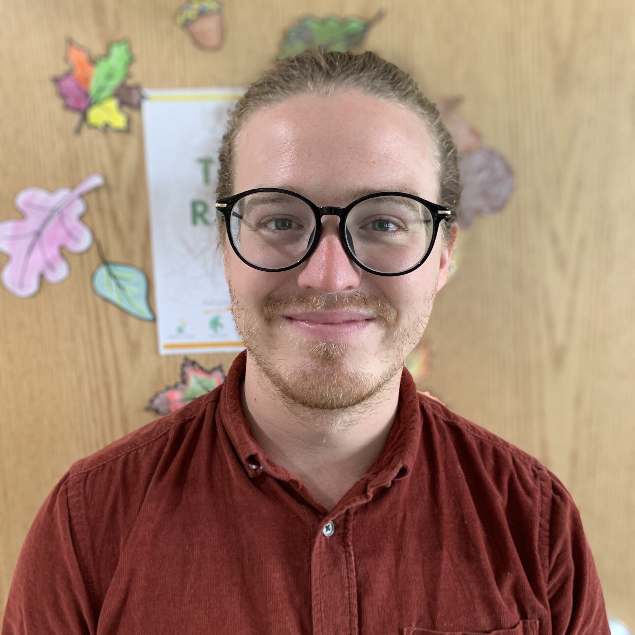 Smiling portrait of Liam Regan, who has a light skin tone, tied-back blond hair, and glasses.